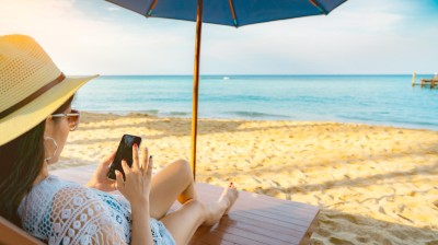 Frau mit Hut sitzt am Sandstrand unter Sonnenschirm