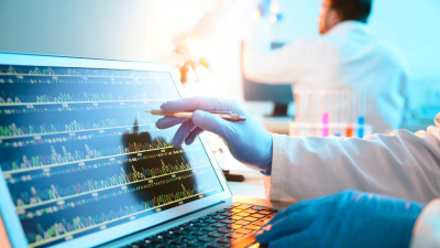Image is a photograph of a scientist looking at a DNA sequence on a laptop