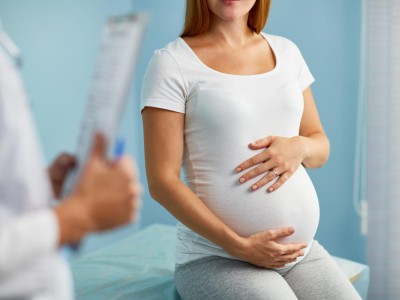 Schwangere sitzt und hält die Hände an den Bauch