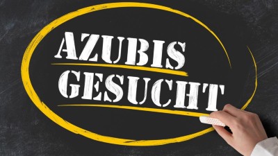 Hand, die ein Stück Kreide gegen eine Tafel mit der Aufschrift "AZUBIS GESUCHT" hält. 