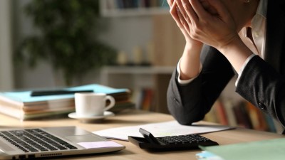 Jemand sitzt am Arbeitsplatz vor einem Laptop und hält sich die Hände vor sein Gesicht