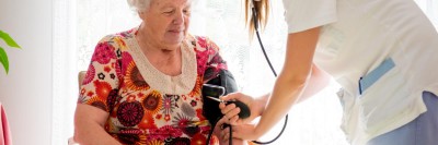 Junge Frau misst Blutdruck bei älterer Frau