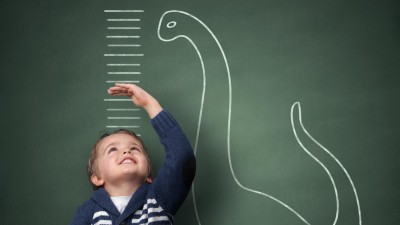 Kleiner Junge steht vor Wand mit Messlatte und Dinosaurier