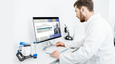 Arzt sitzt am Tisch vor einem Bildschirm mit Tastatur. Neben dem Bildschirm steht ein zahnmedizinischer Artikulator