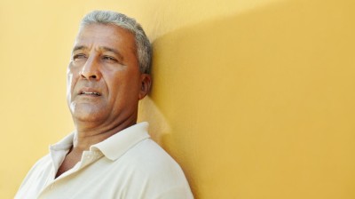 Älterer Mann lehnt an gelber Wand und schaut traurig