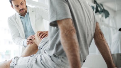 Arzt untersucht Knie eines Senioren