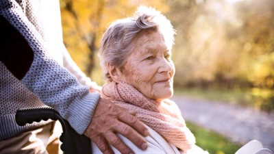 Unrecognizable senior man and elderly woman in wheelchair in autumn nature. Man with his mother on a walk.