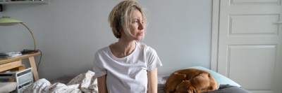 Frau sitzt auf eine Bett und schaut zur Seite
