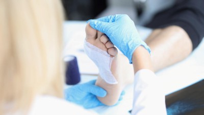 Ärztin untersucht verbundene Wunde am Fuß