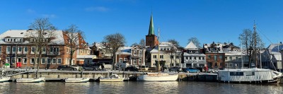 Hafenansicht von neustadt: mehrere kleine Boote liegen vertäut an der Kaimauer. Dahinter sind mehrere Gebäude aus zumeist roten Zieglsteinen sowie eine Kirche mit grünlicher Turmspitze zusehen.