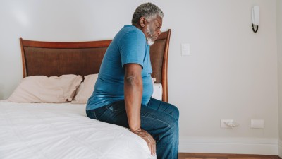 Older man with overweight sitting on the edge of a bed and looks unhappy