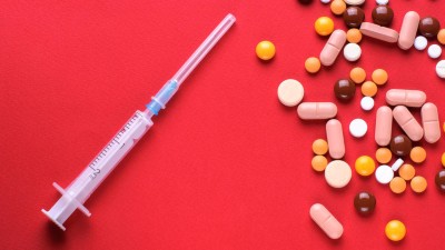 Syringe and multicolored pills on red background
