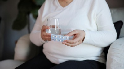 Woman holding a strip of white pills and a glass of water