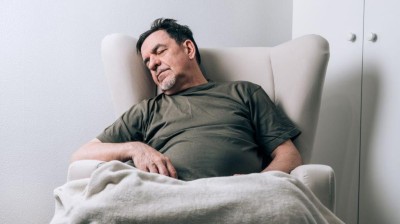 This image is a photograph of a man with a swollen-looking abdomen resting in an armchair