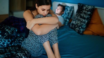Traurige Frau sitzt auf dem Bett mit Partner im Hintergrund