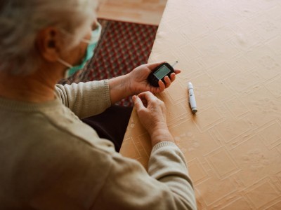 Ältere Frau am Tisch misst Blutzucker