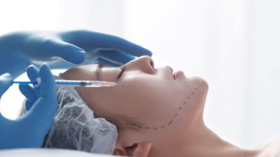 Image is a close-up photograph of a young woman receiving a facial injection