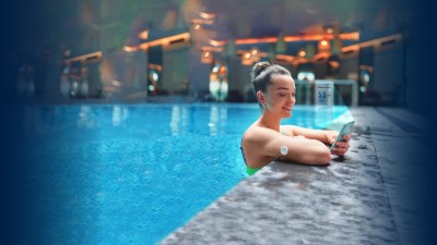 Woman monitoring glucose level with sensor and an app on her phone while training at swimming pool 