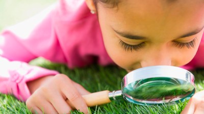 Mädchen guckt sich Rasen durch ein Vergrößerungsglas an