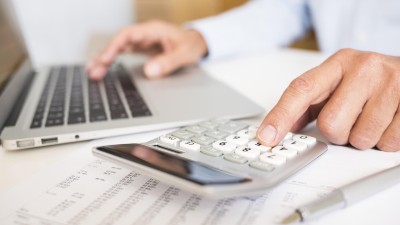 Mann sitzt am Laptop und nutzt einen Taschenrechner