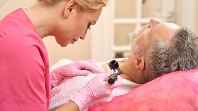Doctor examining man's neck with a dermatoscope