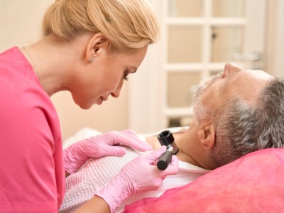 Doctor examining man's neck with a dermatoscope