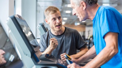 This image is a photo of an elderly man on a treadmill being cheered on by a personal trainer