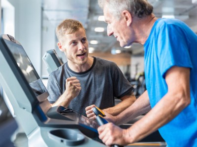 This image is a photo of an elderly man on a treadmill being cheered on by a personal trainer