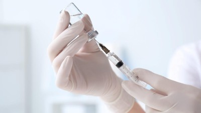 Close-up of gloved hand filling syringe from a vial