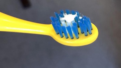 Gelbe Zahnbürste mit etwas weißlicher Zahnpasta auf den blauen Borsten