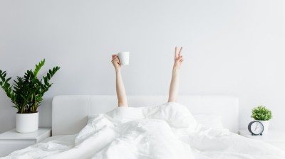Person im Bett unter der Bettdecke streckt Arme empor