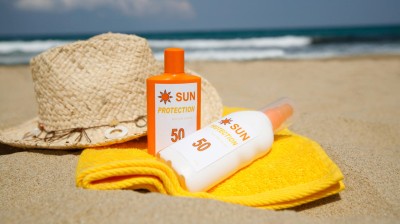 Sonnencreme, Sonnenhut und Handtuch am Strand