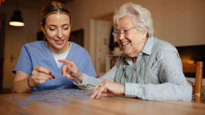 Pflegekraft hilft Bewohnerin beim Puzzle