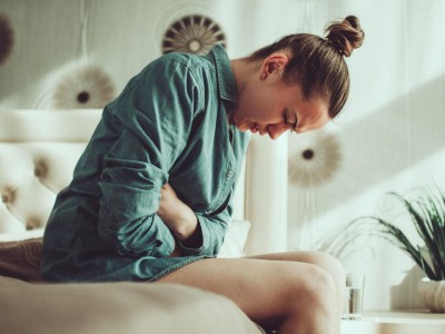 Junge Frau sitz auf dem Bett und hält sich den Bauch