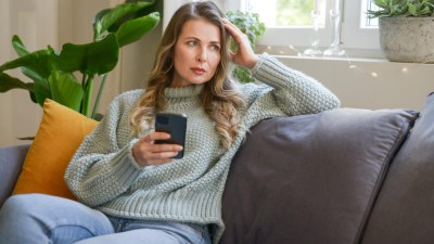 Frau sitzt mit Smartphone in der Hand auf dem Sofa