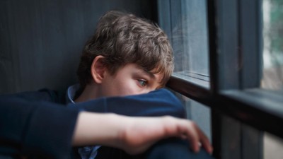 Kind sieht traurig aus dem Fenster