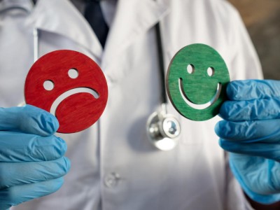 Arztperson mit blauen Handschuhen hält einen roten und einen grünen Smiley in den Händen