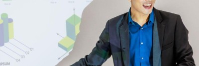 Junger Mann deutet lächelnd mit einem Stift auf eine Präsentationsfolie.