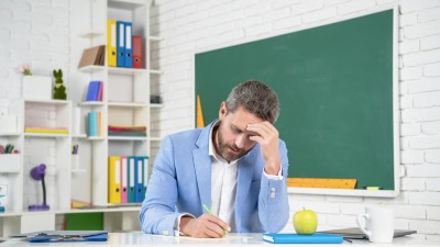 Lehrer sitzt im Klassenraum an einem Schreibtisch