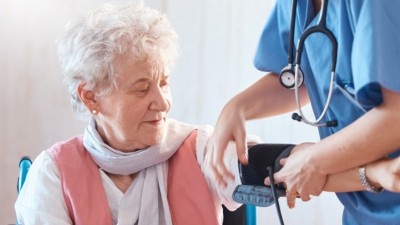 Einer älteren Frau im Rollstuhl wird der Blutdruck gemessen