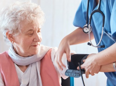 Einer älteren Frau im Rollstuhl wird der Blutdruck gemessen