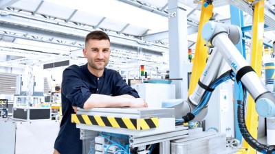 Paul Motzki, ein junger Mann mit kurzem Haar, vor einem großen Roboterarm