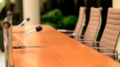 Sitzungssaal mit Mikrofonen vor drei Stühlen