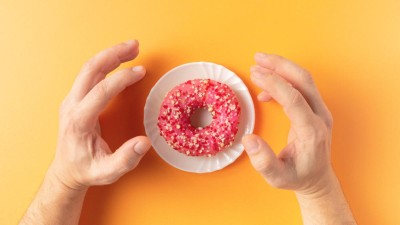 Image is a photograph of hands reaching for a donut
