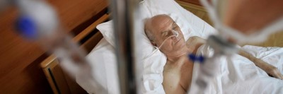 Älterer Mann im Krankenhausbett hinter Infusionsständer