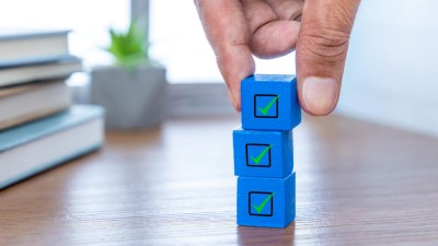 Hand stacking three blue wooden blocks with green checkmarks