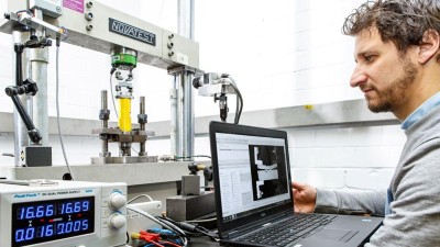 Ein Mann sitzt an einem Tisch und arbeitet an einem Laptop, der mit einer Prüfmaschine verbunden ist.