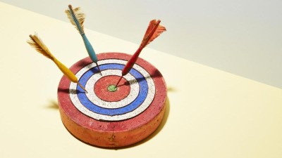 Three darts in a dart board with one hitting the bull's-eye