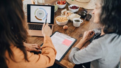 Ernährungsberaterin im Gespräch mit älterer Frau am Esstisch, auf dem Laptop und Nahrungsmittel stehen