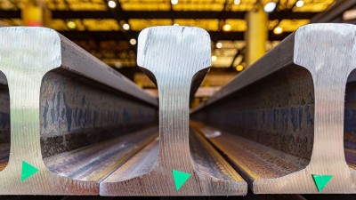 Nahaufnahme von drei massiven Stahl-Schienenprofilen, die nebeneinander in einer Halle liegen.